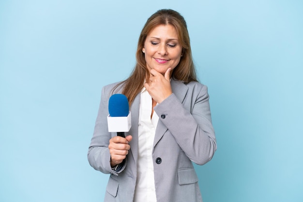 Femme d'âge mûr présentatrice de télévision sur fond bleu isolé regardant sur le côté et souriant