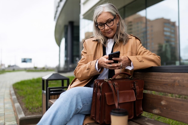 Une femme âgée adulte âgée est assise dans un parc dans la rue et lit un message sur un téléphone mobile