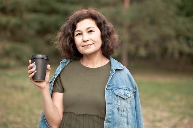 Femme âgée d'âge moyen marchant dans un parc en plein air et buvant du café