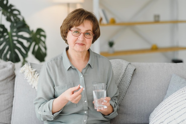 Femme âgée d'âge moyen mature tenant une pilule et un verre d'eau prenant un analgésique pour soulager la douleur suppléments de médicaments vitamines antibiotiques médicaments pour personnes âgées concept vue rapprochée