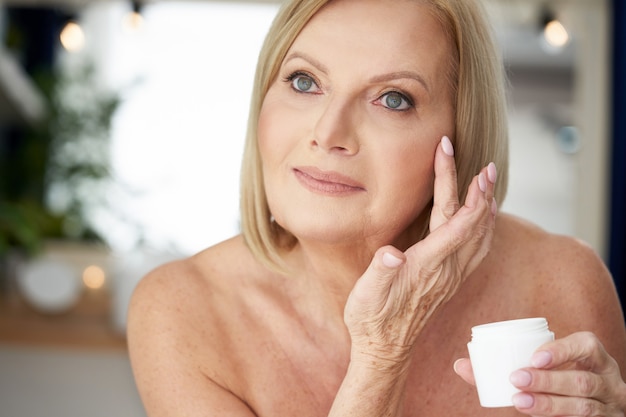 femme âgée, appliquer la crème pour le visage dans la salle de bain