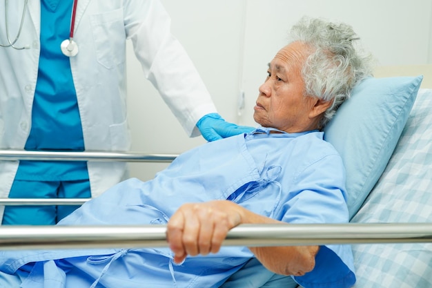 Une femme âgée asiatique âgée patiente tenant une barrière de lit tout en se couchant avec espoir en attendant sa famille à l'hôpital