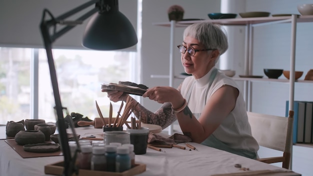 Femme âgée asiatique appréciant le travail de poterie à la maison Une femme céramiste fabrique de nouvelles poteries dans un studio