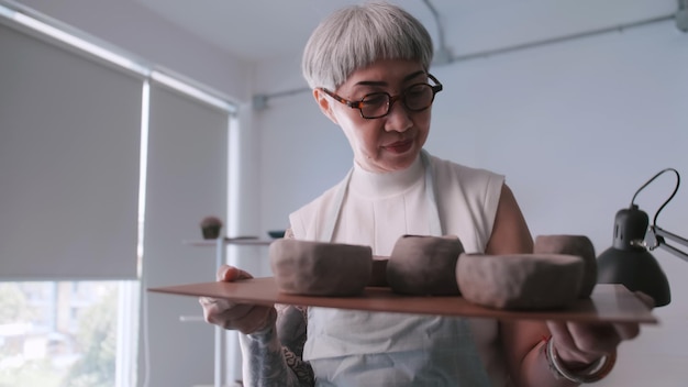 Femme âgée asiatique appréciant le travail de poterie à la maison Une femme céramiste fabrique de nouvelles poteries dans un studio