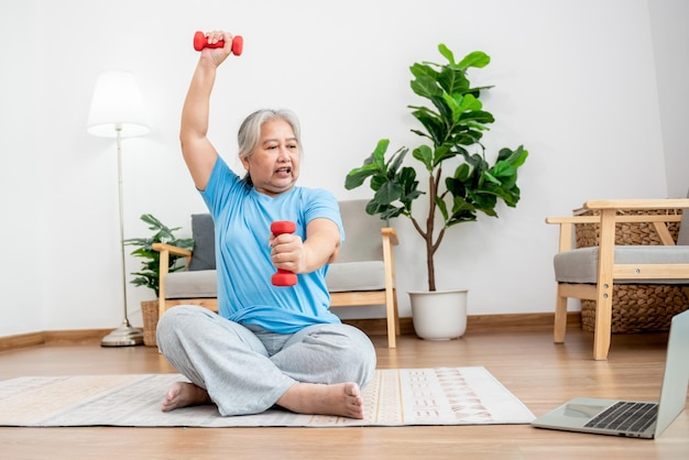 Femme âgée asiatique faisant de l'exercice à la maison en étirant les muscles du bras et en utilisant un haltère