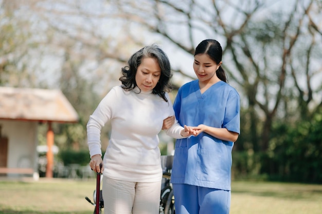 Femme âgée asiatique en fauteuil roulant avec un soignant asiatique attentif concept de jardin d'hôpital de maison de retraite à la lumière du soleil