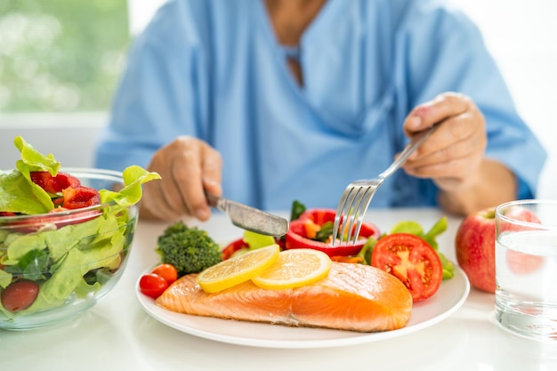 Une femme âgée asiatique patiente mangeant un petit-déjeuner de steak de saumon avec des aliments sains à base de légumes à l'hôpital