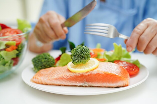 Une femme âgée asiatique patiente mangeant un pieu de saumon et une salade de légumes pour une alimentation saine à l'hôpital