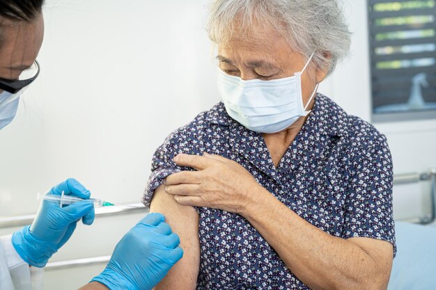 Une femme âgée asiatique portant un masque facial reçoit un vaccin contre le covid-19 ou le coronavirus par un médecin fait une injection.