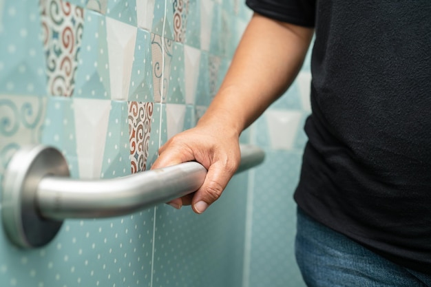 Une femme âgée asiatique utilise la poignée de la salle de bain pour la sécurité dans les toilettes.