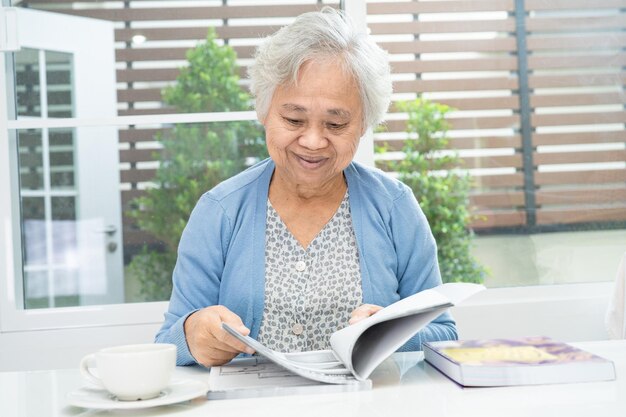 Femme âgée asiatique ou vieille dame âgée lisant un livre pour pratiquer le cerveau tout en vivant à la maison, concept de retraite de passe-temps au repos.