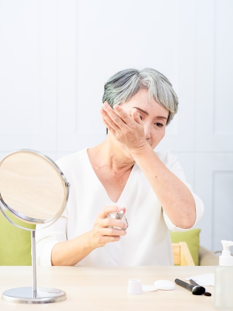 Une femme âgée d'Asie vaporise du parfum à la maison.