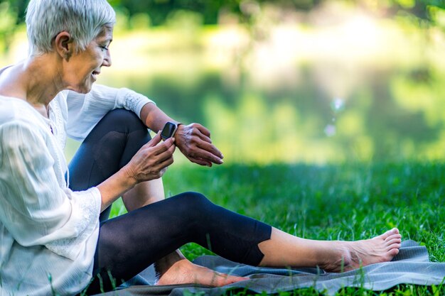 Femme âgée assise au bord de l'eau définissant son application de montre intelligente de méditation