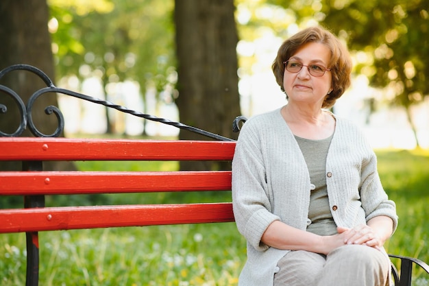 Une femme âgée assise sur un banc dans le parc d'été