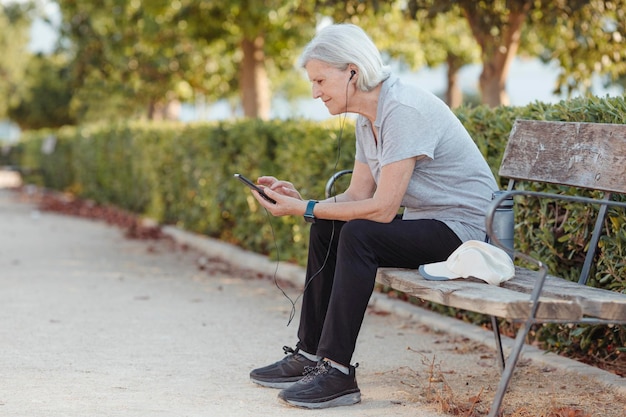 Une femme âgée assise sur un banc de parc regarde son téléphone