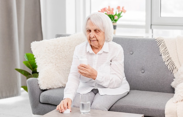 Femme âgée assise sur le canapé et regardant l'emballage des pilules à la maison