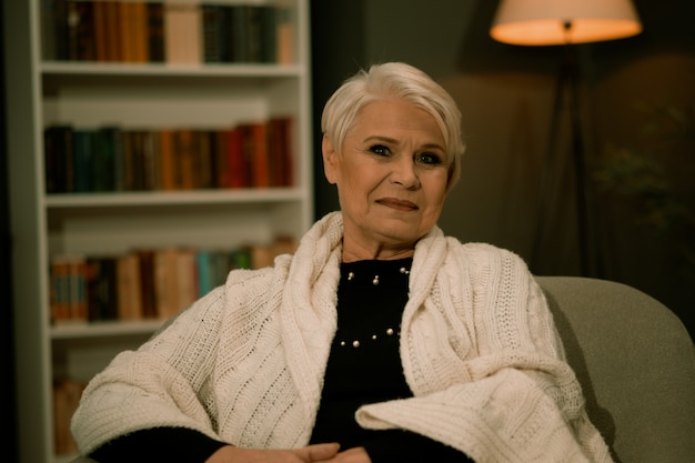 Femme âgée assise sur une chaise dans une chambre confortable