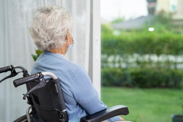 Une femme âgée assise sur un fauteuil roulant regarde par la fenêtre pour attendre quelqu'un. Tristement, mélancolique et déprimé.