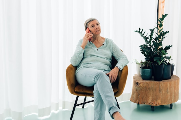 Femme âgée assise à la maison ayant une conversation téléphonique à l'aide d'un smartphone