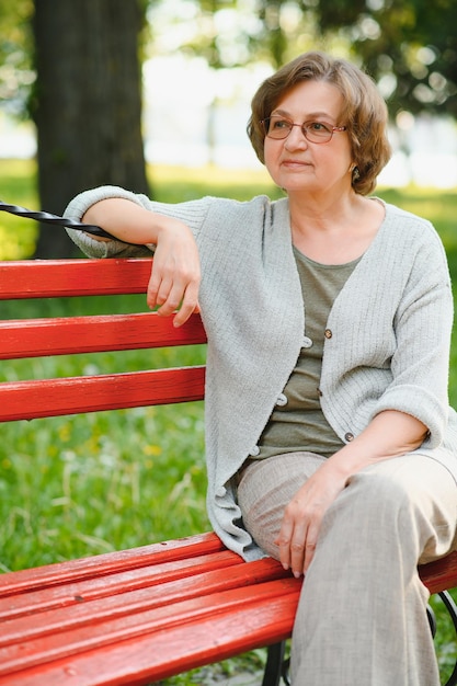 Femme âgée assise et relaxante sur un banc à l'extérieur dans le parc