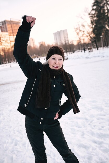 femme âgée au chapeau et veste sportive faisant des exercices sportifs dans le parc d'hiver de neige.