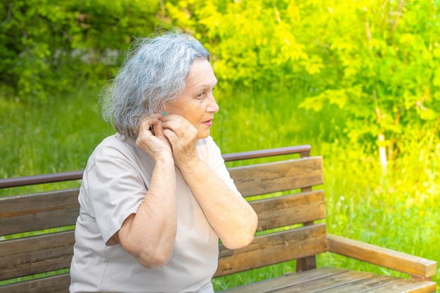Une femme âgée aux cheveux gris ajuste sa boucle d'oreille alors qu'il était assis sur un banc de parc