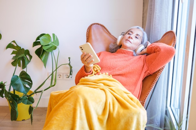 Femme âgée aux cheveux gris assis détendu en écoutant de la musique depuis son smartphone et ses écouteurs Musique de repos de retraite Concept