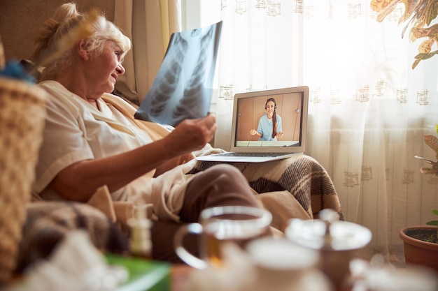 Femme âgée ayant une consultation en ligne avec un médecin à la maison