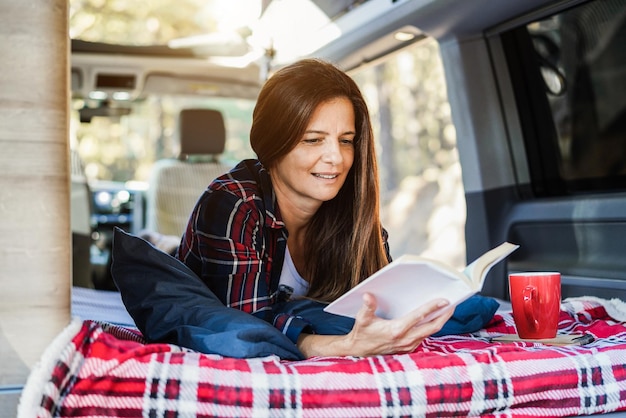 Femme âgée ayant à l'intérieur du camping-car en lisant un livre et en buvant du café - Focus on face