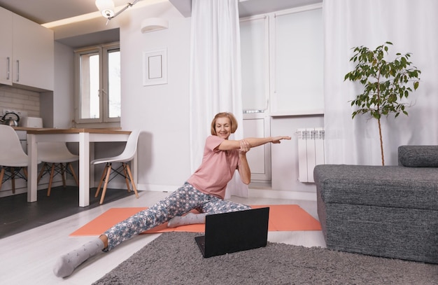 Une femme âgée, une blogueuse engagée dans des cours de yoga en ligne à domicile est le concept d'un mode de vie sain pour les personnes âgées.