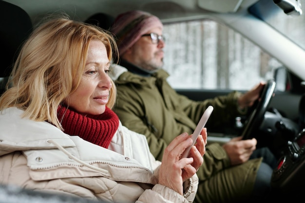 Femme âgée blonde en vêtements d'hiver textos sur smartphone