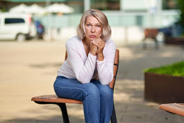 Femme âgée bouleversée assise sur un banc dans la rue.