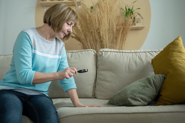 Femme âgée bouleversée examine les taches sur un canapé avec une loupe