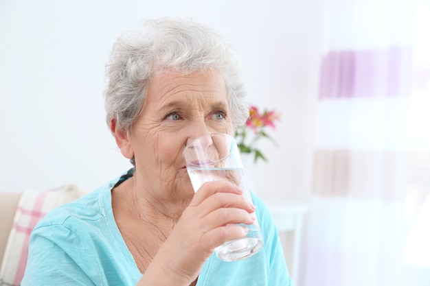 Femme âgée buvant de l'eau à la maison. Concept de retraite