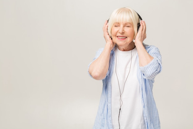 Femme âgée avec un casque d'écoute de la musique sur un téléphone isolé sur fond blanc