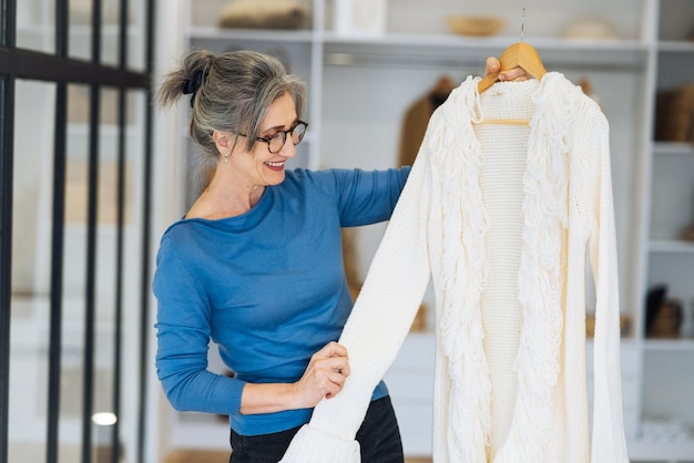 Une femme âgée choisit un pull blanc à la maison