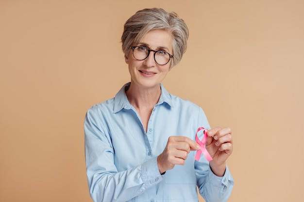 Femme âgée confiante tenant un ruban rose isolé sur fond beige Sensibilisation au cancer du sein