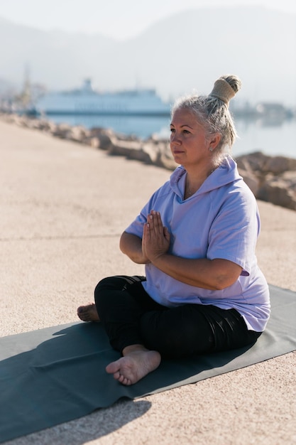 Femme âgée consciente avec des dreadlocks méditant au bord de la mer et de la pratique du yoga et du bien-être à la plage