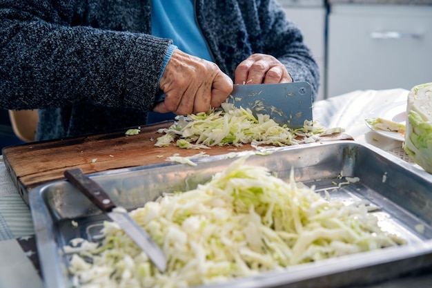 Femme âgée coupant du chou sur une planche à découper en bois dans la vue des mains de la cuisine