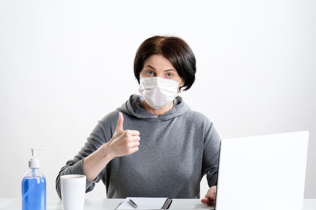 femme âgée dans un masque de protection fonctionne sur un ordinateur. Femme dans un masque médical sur le lieu de travail.