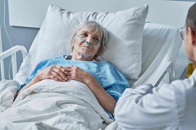 Femme âgée dans un tube à oxygène dans le nez allongée sur le lit dans le service et ayant un traitement à l'hôpital avec son médecin