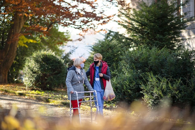 Femme âgée avec déambulateur et soignant ou travailleur de la santé à l'extérieur lors d'une promenade dans le parc, concept de coronavirus.