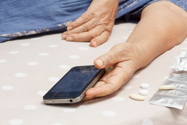 Femme âgée dormant dans son lit et tenant un téléphone portable.