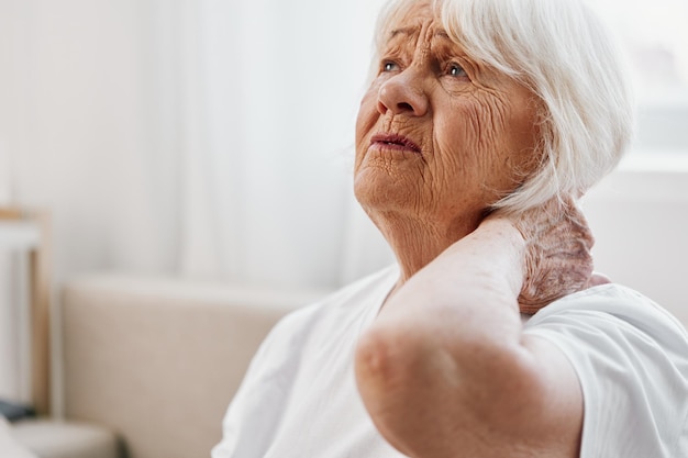 Photo femme âgée douleur au cou sévère assise sur le canapé problèmes de santé dans la vieillesse mauvaise qualité de vie