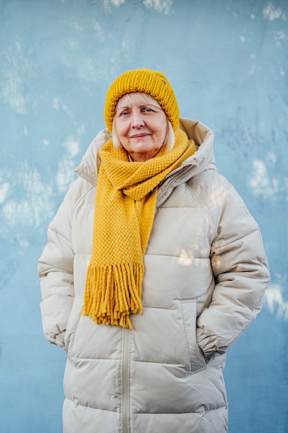 Femme âgée élégante en manteau chaud avec écharpe tricotée jaune et chapeau