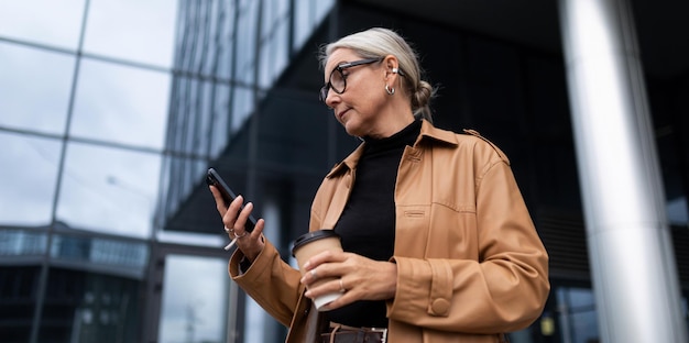 Femme agée élégante avec un téléphone portable et un verre de café sur le fond d'un moderne