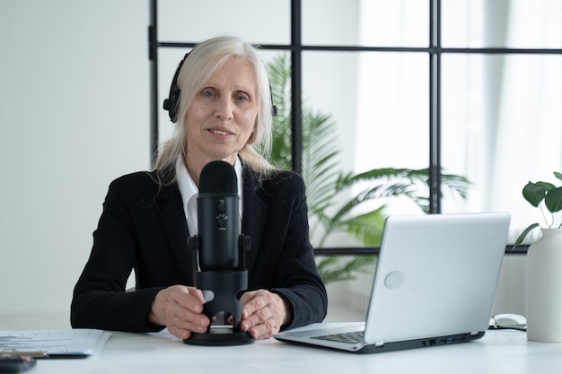Une femme âgée enregistre un podcast sur son ordinateur portable avec des écouteurs et un microphone
