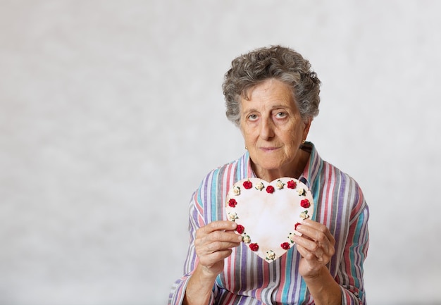 Une femme âgée entre 70 et 80 ans garde le cœur entre les mains. Fond gris