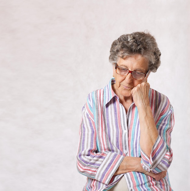 Une femme âgée entre 70 et 80 ans pense à quelque chose. Fond gris