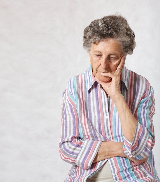 Une femme âgée entre 70 et 80 ans pense à quelque chose. Fond gris